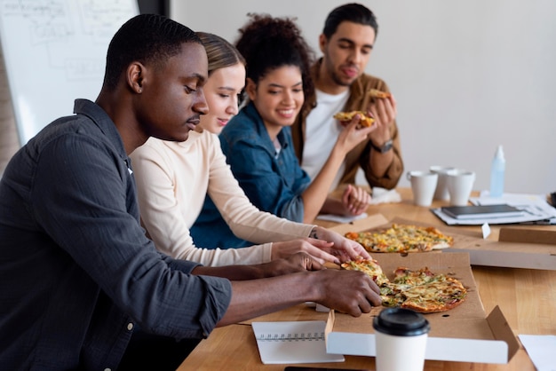 Free photo medium shot people eating pizza at work