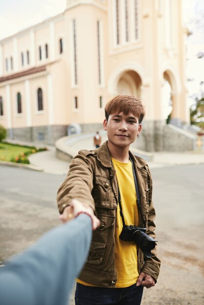 Medium shot portrait of an Asian guy with photo camera holding hand of unrecognizable woman