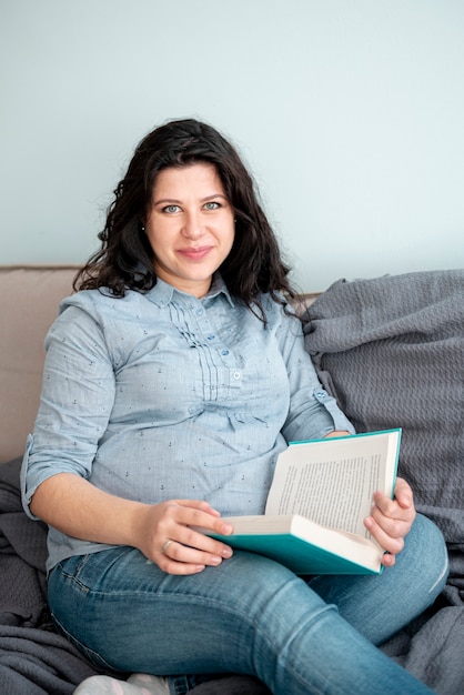 Medium shot pregnant woman laying on the couch with book