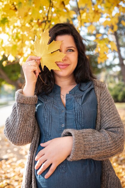 Medium shot pregnant woman posing with leaf