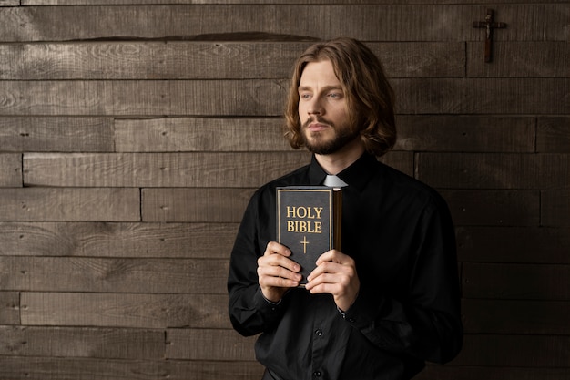 Free photo medium shot priest holding holy bible