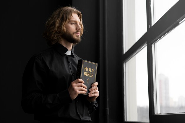 Medium shot priest holding holy bible