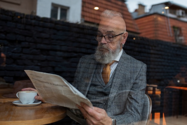 カフェで読書するミディアムショットのシニア男性