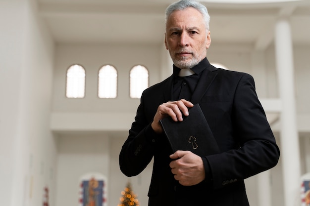 Medium shot senior priest holding bible