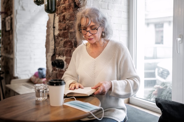 Medium shot senior woman reading at coffee shop