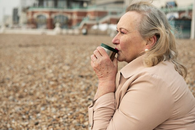 Medium shot senior woman with drink at beach