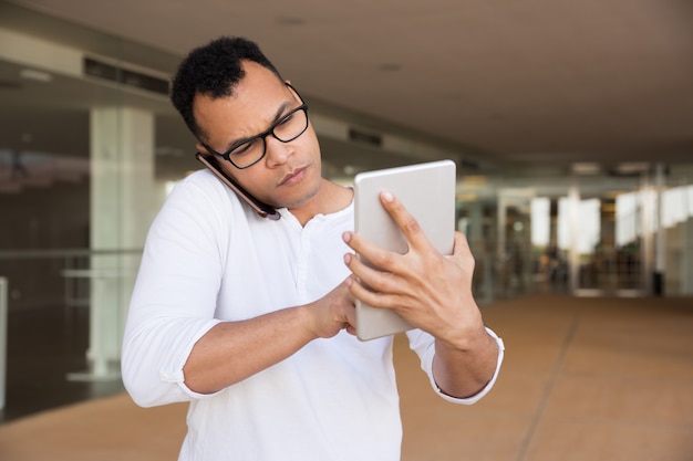 タブレットに取り組んでいる、電話で話している深刻な男のミディアムショット