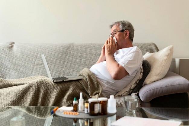 medium shot sick man on couch with laptop