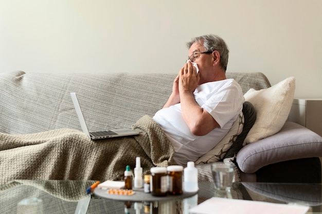 Medium shot sick man on couch with laptop