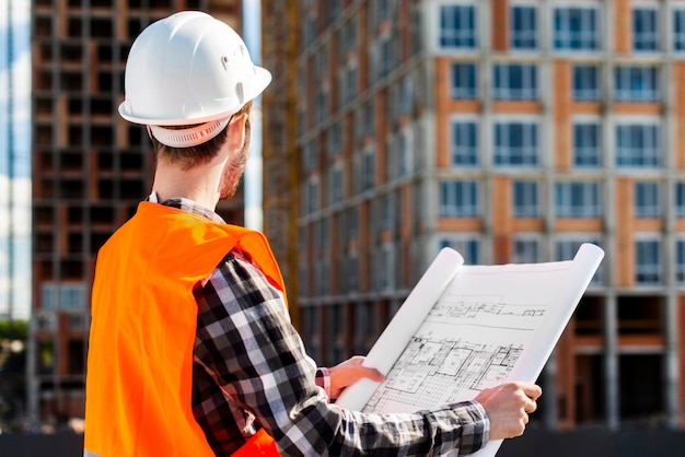 Medium shot side view of engineer holding plans