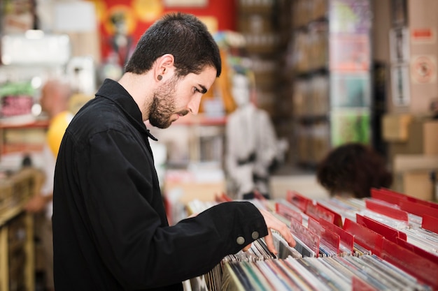 Medium shot side view of young man looking for vinyls in store