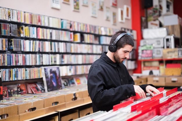 Medium shot side view of young man looking for vinyls in store