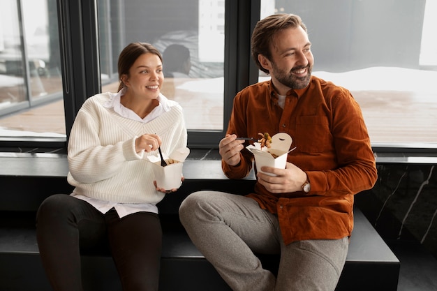 Medium shot smiley colleagues eating noodles