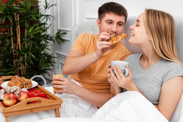 Medium shot smiley couple having breakfast in bedroom