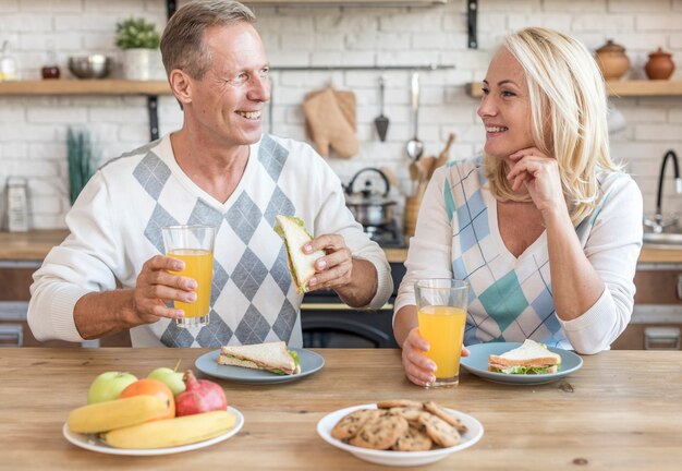 Medium shot smiley couple in the kitchen having breakfast