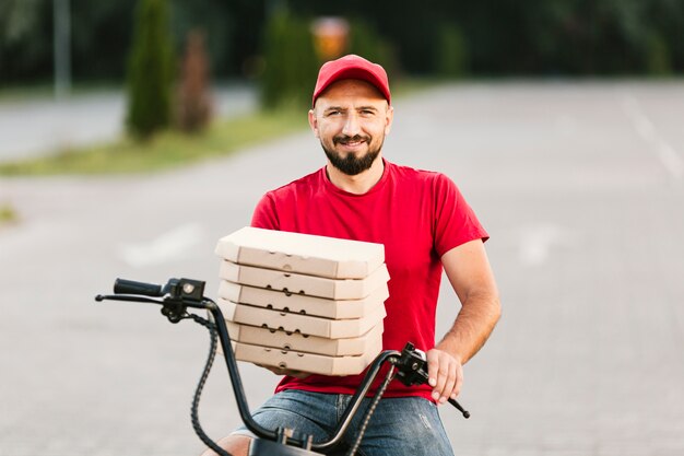 Medium shot smiley delivery guy holding pizza boxes