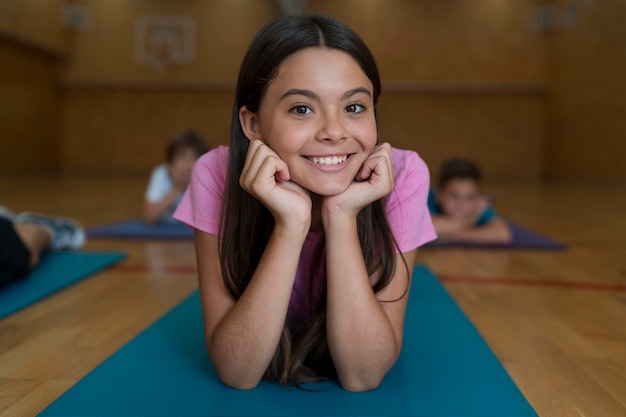 Бесплатное фото Улыбающаяся девочка среднего размера на коврике для йоги