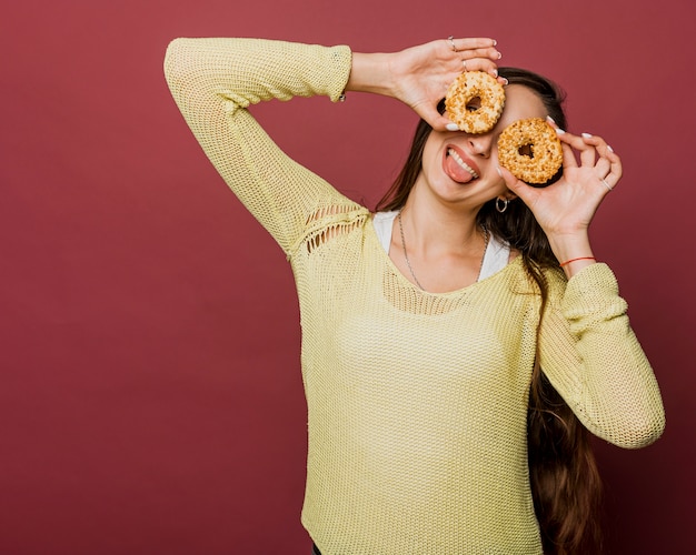 Foto gratuita ragazza di smiley del colpo medio con le ciambelle e la priorità bassa rossa