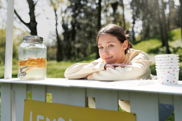 Medium shot smiley girl with lemonade stand outside