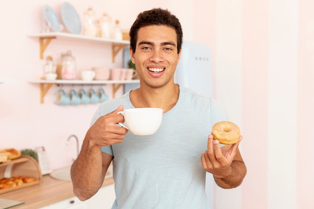 Medium shot smiley man with cup and doughnut