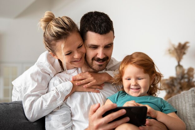 Medium shot smiley parents and kid with phone