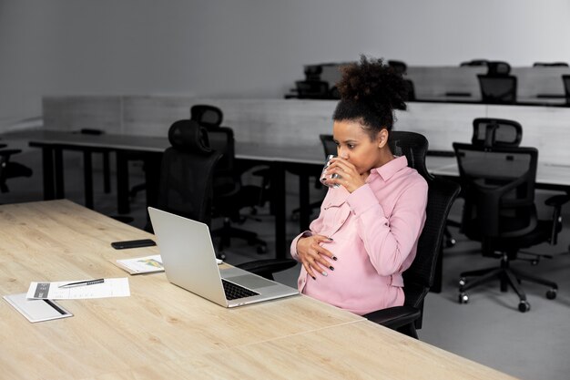 Donna incinta sorridente del colpo medio al lavoro