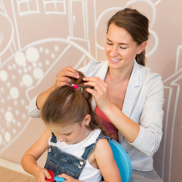 Free photo medium shot smiley teacher tying girl's hair