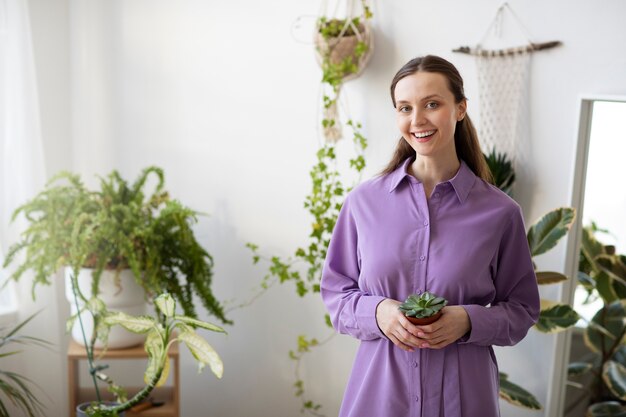 Medium shot smiley woman holding plant at home