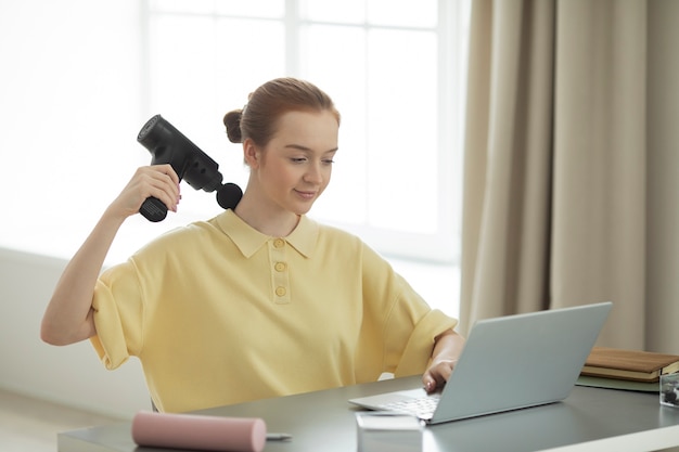 Medium shot smiley woman using massage gun