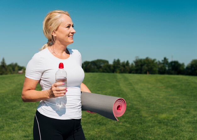 Medium shot smiley woman with yoga mat