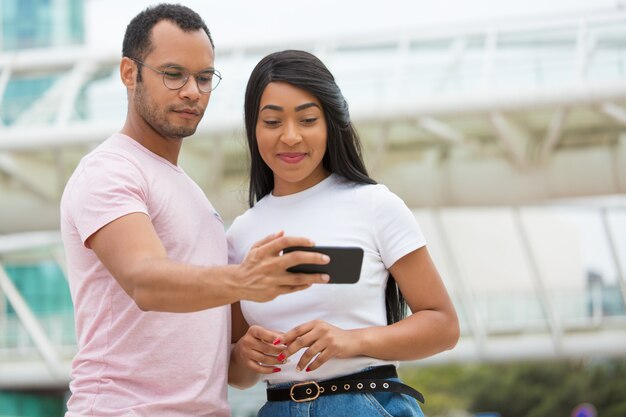 Medium shot of smiling friends looking at smartphone