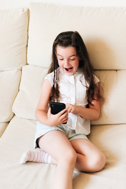 Medium shot surprised girl with phone on the couch