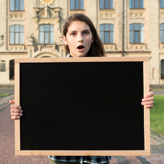 Free photo medium shot surprised highschool girl holding blackboard