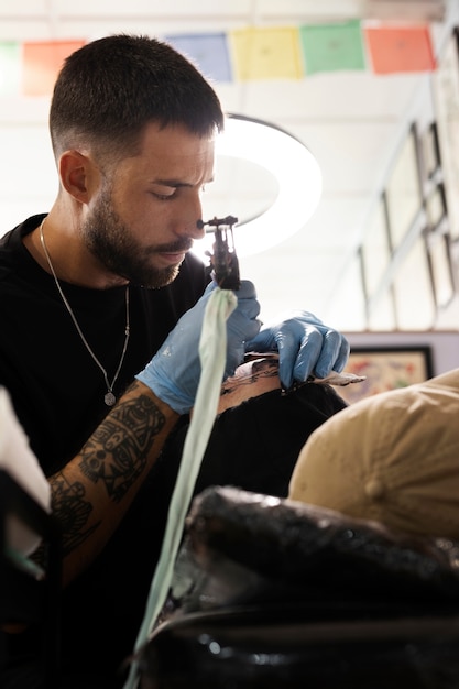 Художник-татуировщик среднего роста делает свою работу