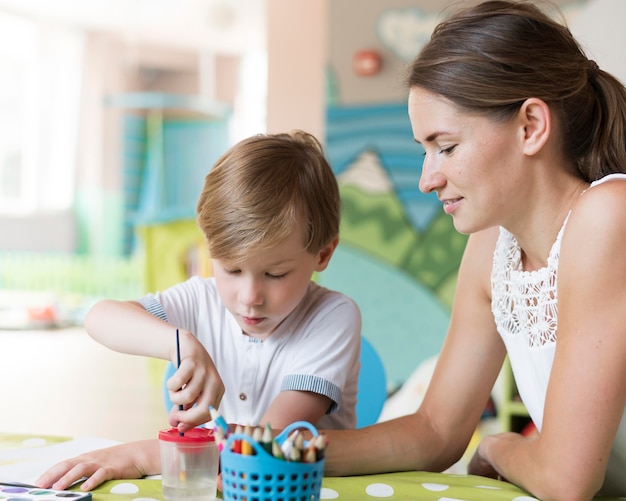 Medium shot teacher and kid painting