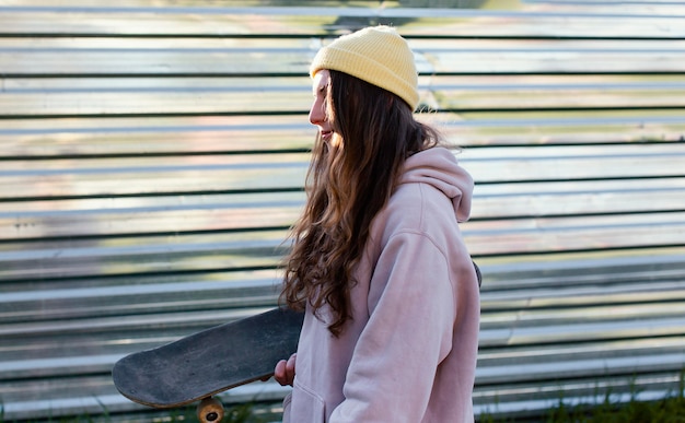スケートボードを保持しているミディアムショットの十代の少女