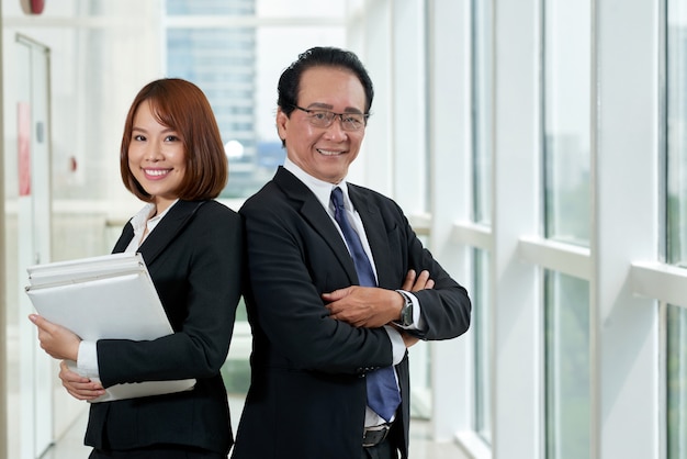 Medium shot of two Asian colleagues standing back to back with their arms folded