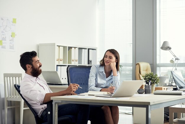 Medium shot of two coworkers sitting at desk and chatting