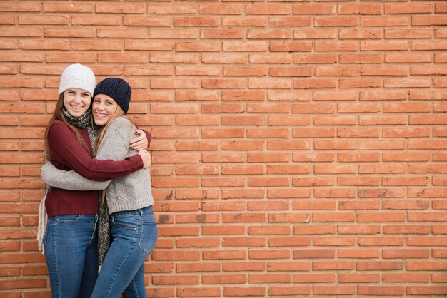 Medium shot two hugging young women in front of brick wall