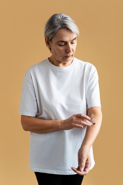 Medium shot woman applying cream on arm