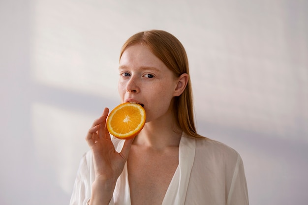 オレンジスライスを噛むミディアムショットの女性