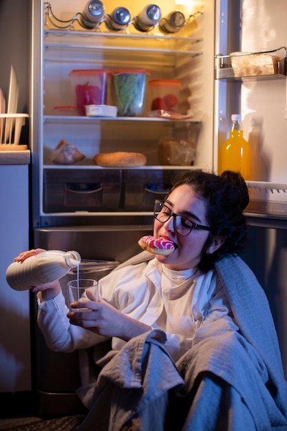 Donna del colpo medio che controlla il frigorifero per uno spuntino