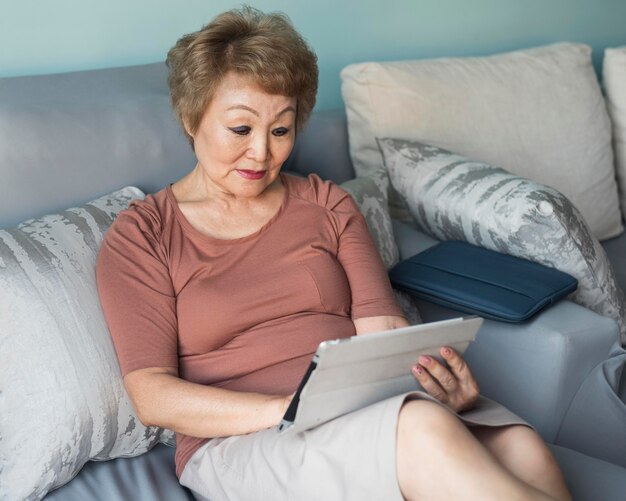 Medium shot woman on couch holding tablet