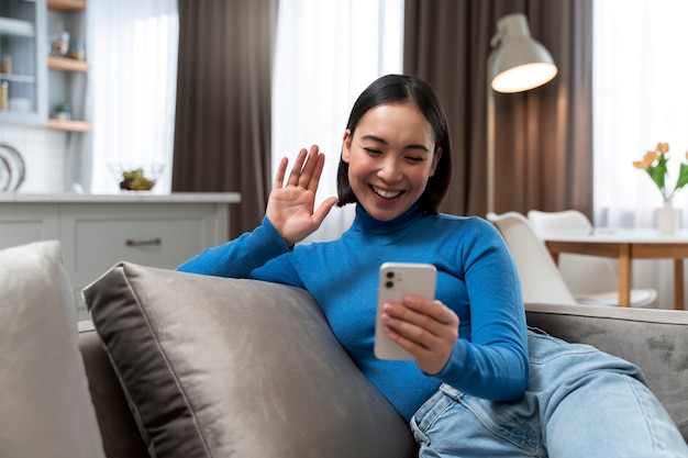 Medium shot woman on couch with smartphone
