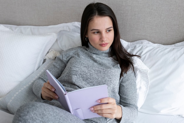 Medium shot woman holding book in bed
