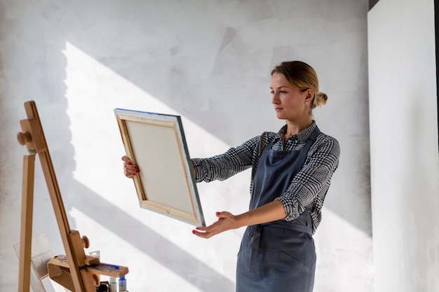Medium shot of woman holding canvas in studio