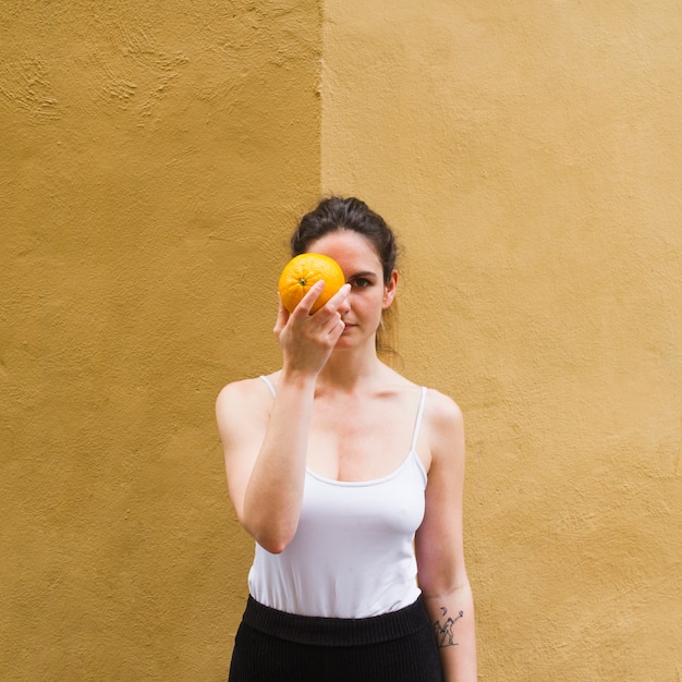 Medium shot woman holding an orange covering her eye