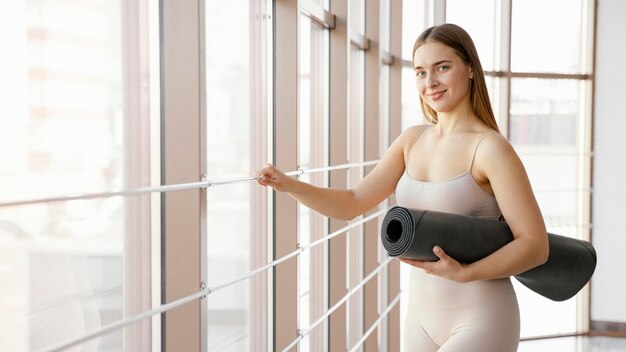 Medium shot woman holding yoga mat