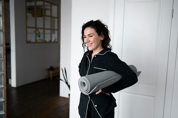 Medium shot woman holding yoga mat