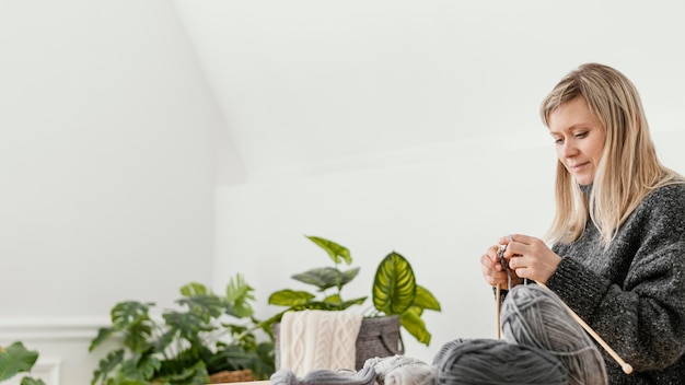 Foto gratuita donna del colpo medio che lavora a maglia all'interno